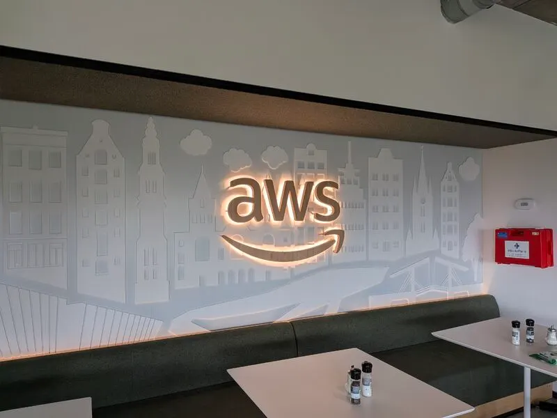 The illuminated AWS logo on a wall illustrated with Amsterdam canal houses, above a lounge seating area.