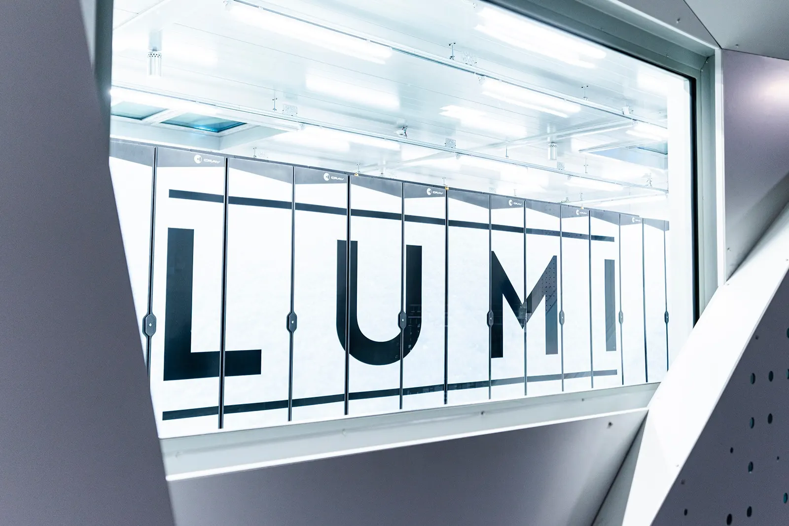 The LUMI supercomputer seen through a window at its data centre in Kajaani, Finland, with the name LUMI printed across a row of Cray cabinets.